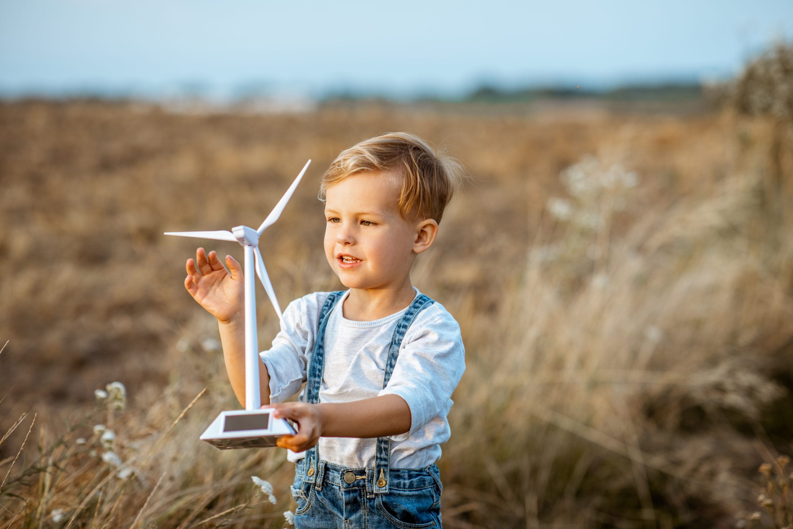 Curious young boy playing with toy wind turbine in the field, studying how green energy works from a young age